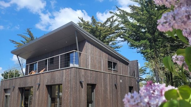 A modern two-story building with a wooden exterior, large windows, and a balcony. - Modern Forest-Edge Home for 10 with WiFi, Close to Beach & Shops (Saint-Jean-de-Monts)