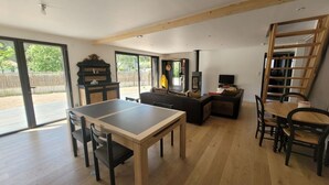 A spacious living area with a wooden table and chairs, a sofa, and a TV. There is a sliding glass door leading to an outdoor patio. - Modern Forest-Edge Home for 10 with WiFi, Close to Beach & Shops (Saint-Jean-de-Monts)