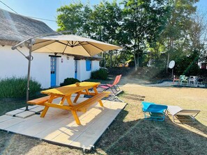 A patio area with a wooden table and benches, a covered seating area, and a small building with blue doors.