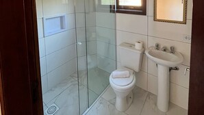A bathroom with a glass shower enclosure, a toilet, and a sink with a mirror above it. - Villa Rural (Campos do Jordão)