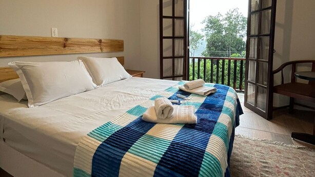 A bedroom with a bed, a wooden headboard, a window with a view, and a balcony. - Villa Rural (Campos do Jordão)