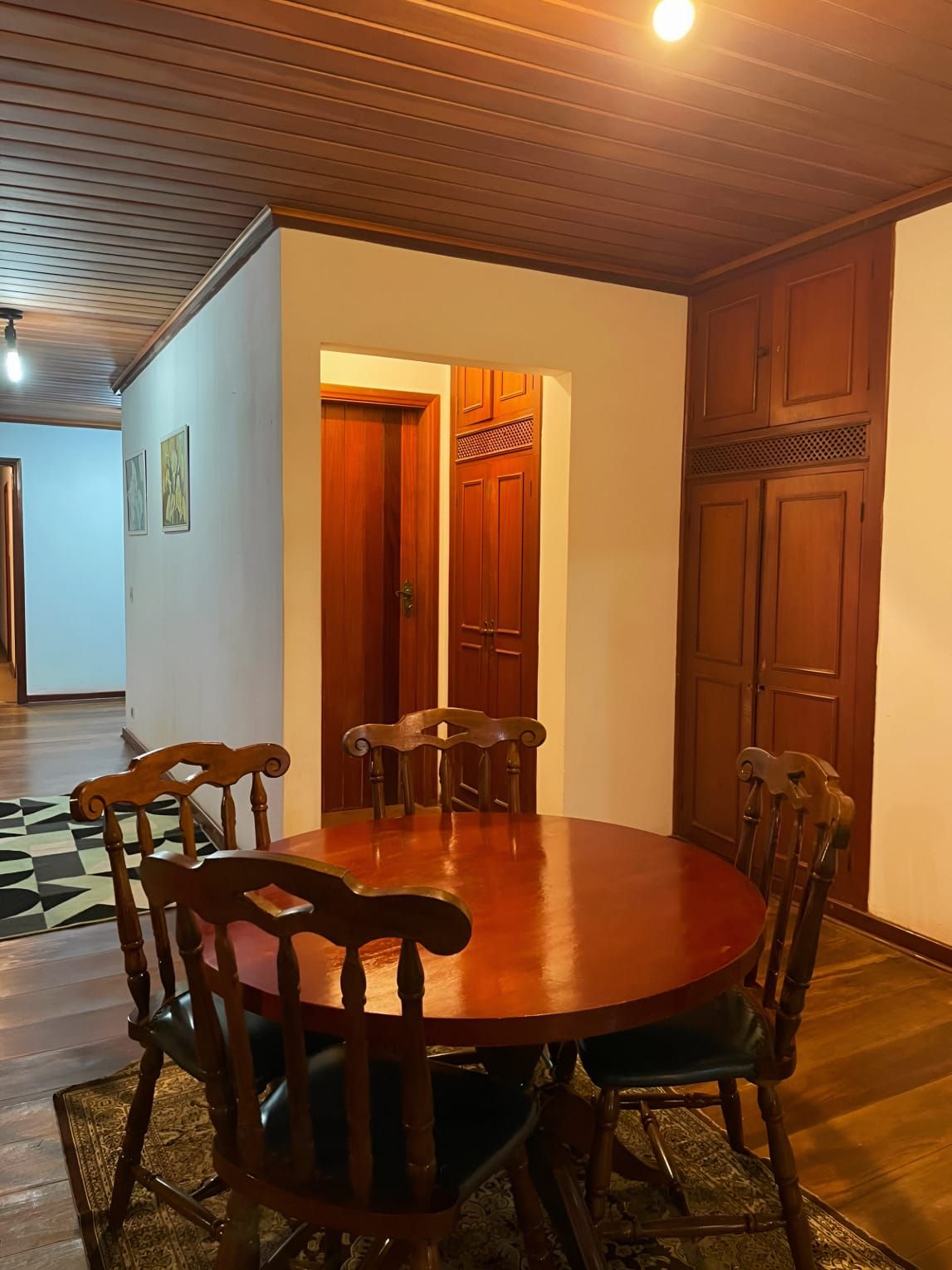 A dining area with a wooden table and chairs, a patterned rug, and wooden doors.