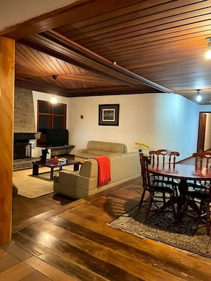 A cozy living room with a fireplace, a sofa, a dining table with chairs, and a stone wall. - Villa Rural (Campos do Jordão)
