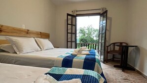 A hotel room with two beds, a wooden headboard, a small table, and a view of greenery through an open door. - Villa Rural (Campos do Jordão)
