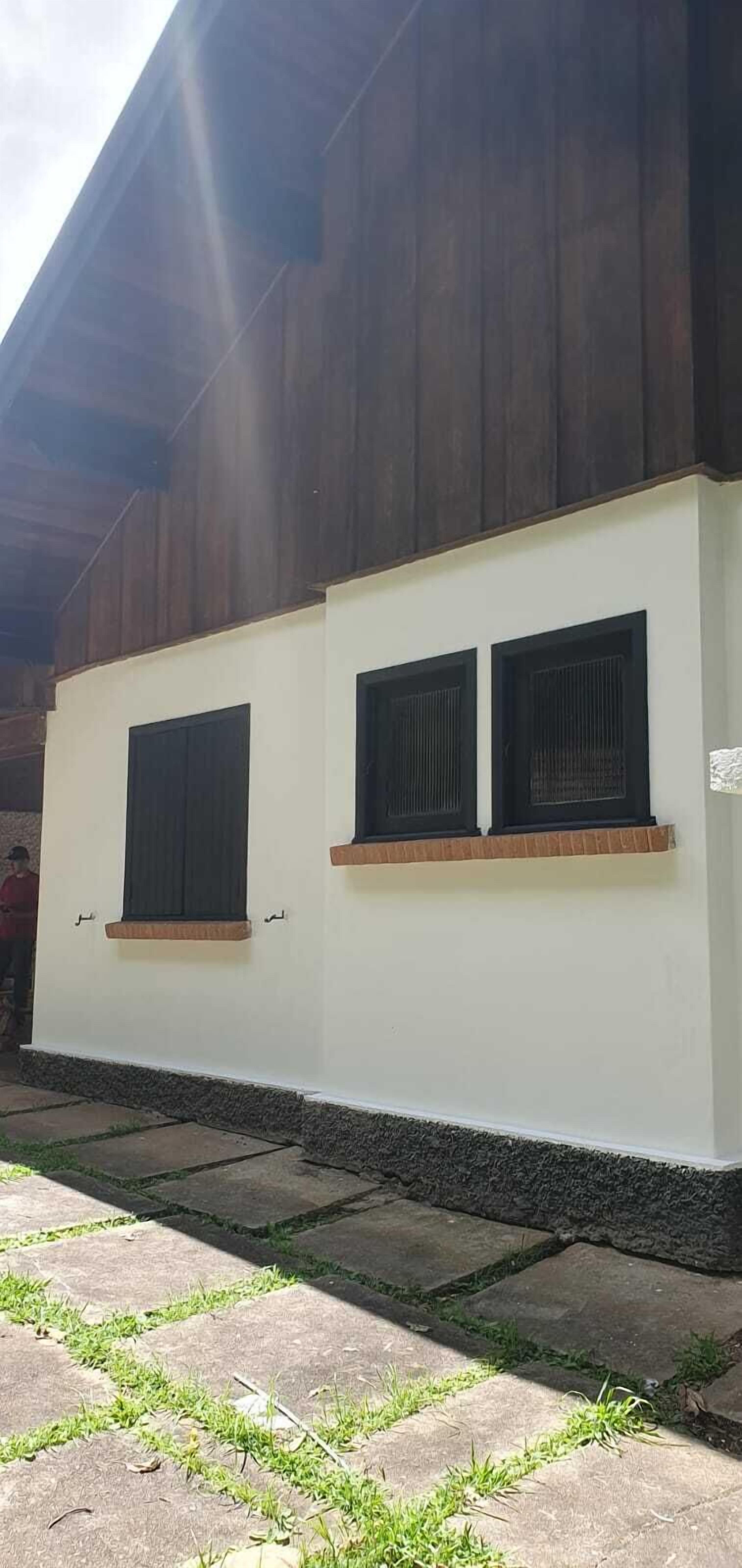 A building with a white exterior and dark wooden siding. There are two windows with black shutters on the white wall.