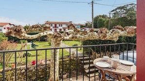 En balkon med udsigt over en have, en stenvæg og en bygning i baggrunden.