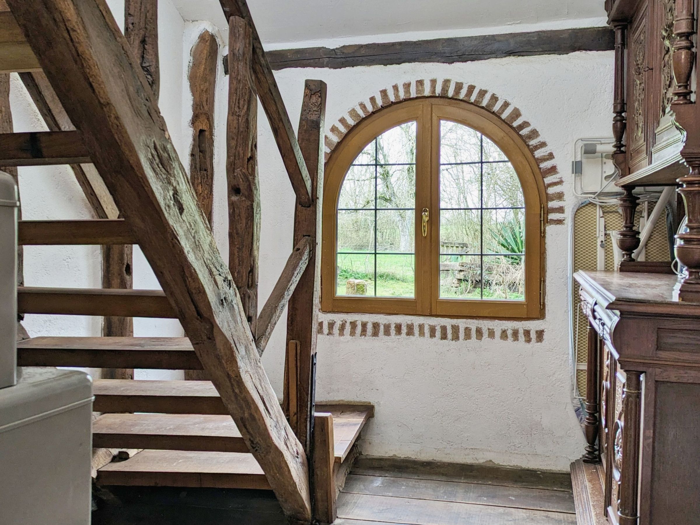 Un escalier en bois mène à une pièce dotée d’une grande fenêtre en arc qui donne sur un jardin.