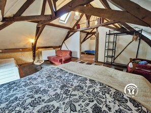 Ein gemütliches Schlafzimmer im Dachgeschoss mit sichtbaren Holzbalken, einem roten Ledersessel, einem kleinen Tisch und einer gemusterten Tagesdecke.