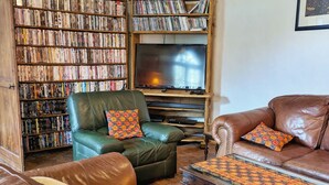 A cozy living room with leather sofas, a coffee table, and a bookshelf filled with DVDs. - Charming Country Retreat: Sleeps 11, Indoor Pool, Pet-Friendly, Near Château-Gontier (Gennes-Longuefuye)
