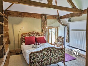 A bedroom with a wooden ceiling, a bed with floral upholstery, red pillows, and a chair with floral upholstery.