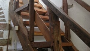 A wooden staircase with a metal handrail, leading to a room with a white brick wall and a small table with a bottle. - Charming Country Retreat: Sleeps 11, Indoor Pool, Pet-Friendly, Near Château-Gontier (Gennes-Longuefuye)