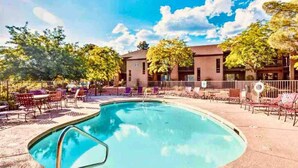 A swimming pool with lounge chairs and tables, surrounded by a fence and trees.
