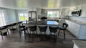 Una cocina moderna con una isla central, taburetes de bar, muebles blancos y vistas al exterior.