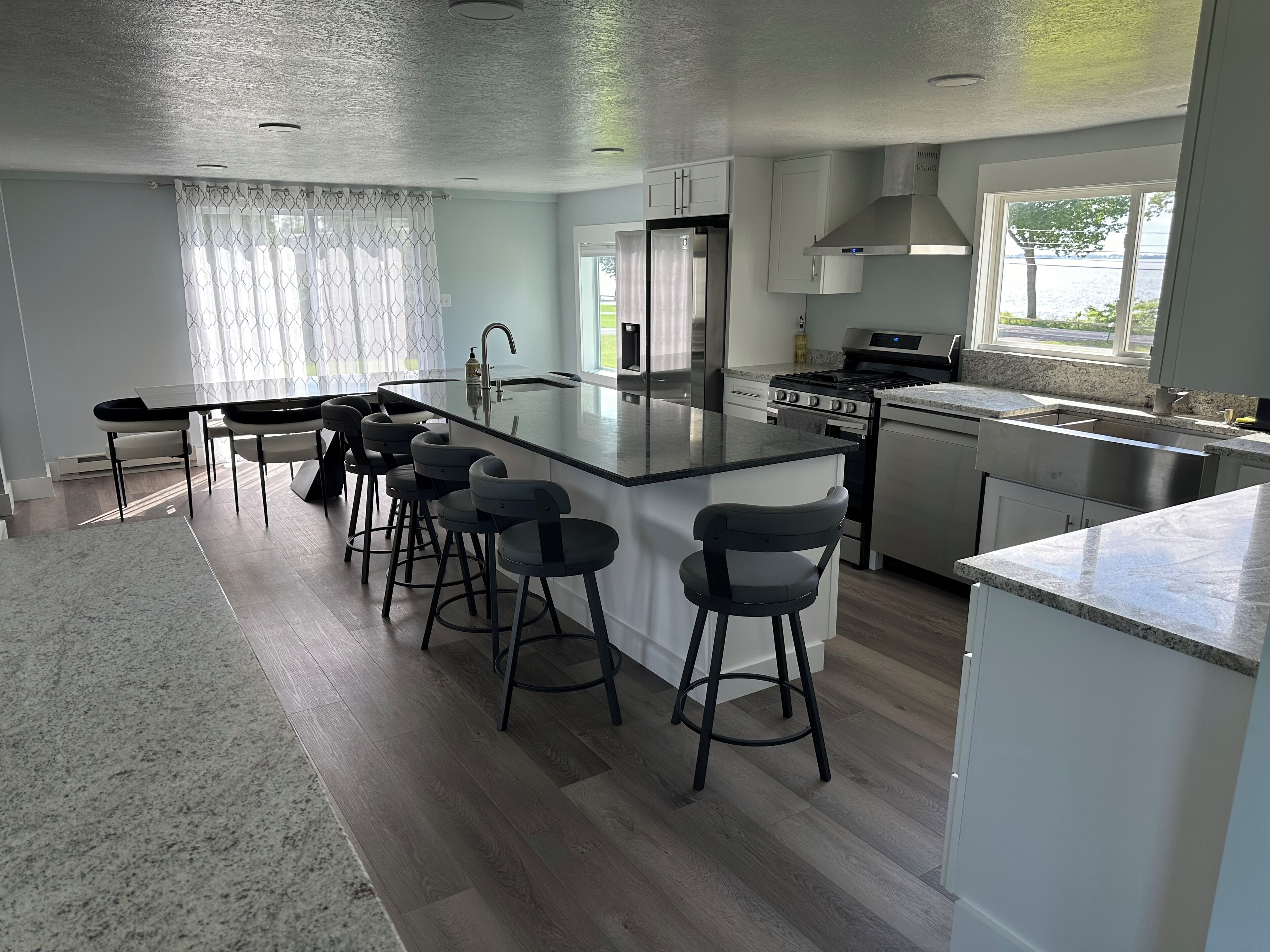 A modern kitchen with a central island, bar stools, stainless steel appliances, and a view of the outdoors.