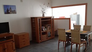 A living room with a wooden coffee table, a television, a bookshelf, and a dining area with chairs and a table. - Gîte de Kerezenn (Fougerolles-Saint-Valbert)