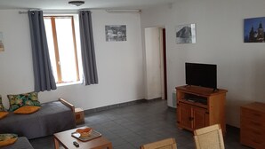 A living room with a sofa, a table, a TV, and a dining area with chairs. - Gîte de Kerezenn (Fougerolles-Saint-Valbert)