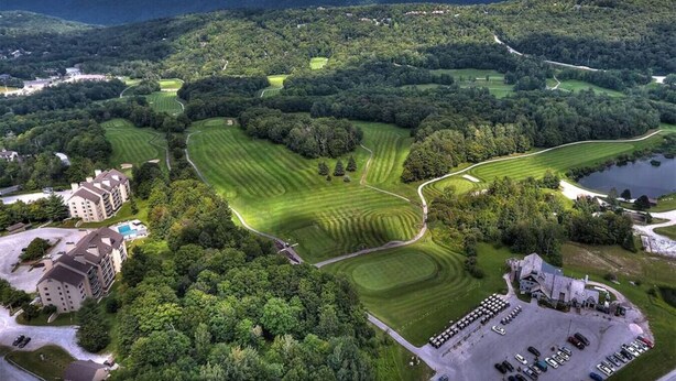 An aerial view of a golf course with a hotel, lush greenery, and a lake. - CountryCub- Pool, Hot Tub, Gym, Sauna, Near Resort (Killington)