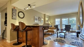 A modern kitchen with a wooden island and bar stools, a dining area with a sofa and chairs, and large windows offering a view of the outdoors. - CountryCub- Pool, Hot Tub, Gym, Sauna, Near Resort (Killington)