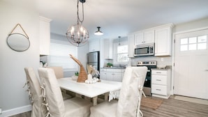 A modern kitchen with white cabinets, stainless steel appliances, and a dining area with a white table and chairs. - Hidden Gem in N. OC on the Beach (Ocean City)