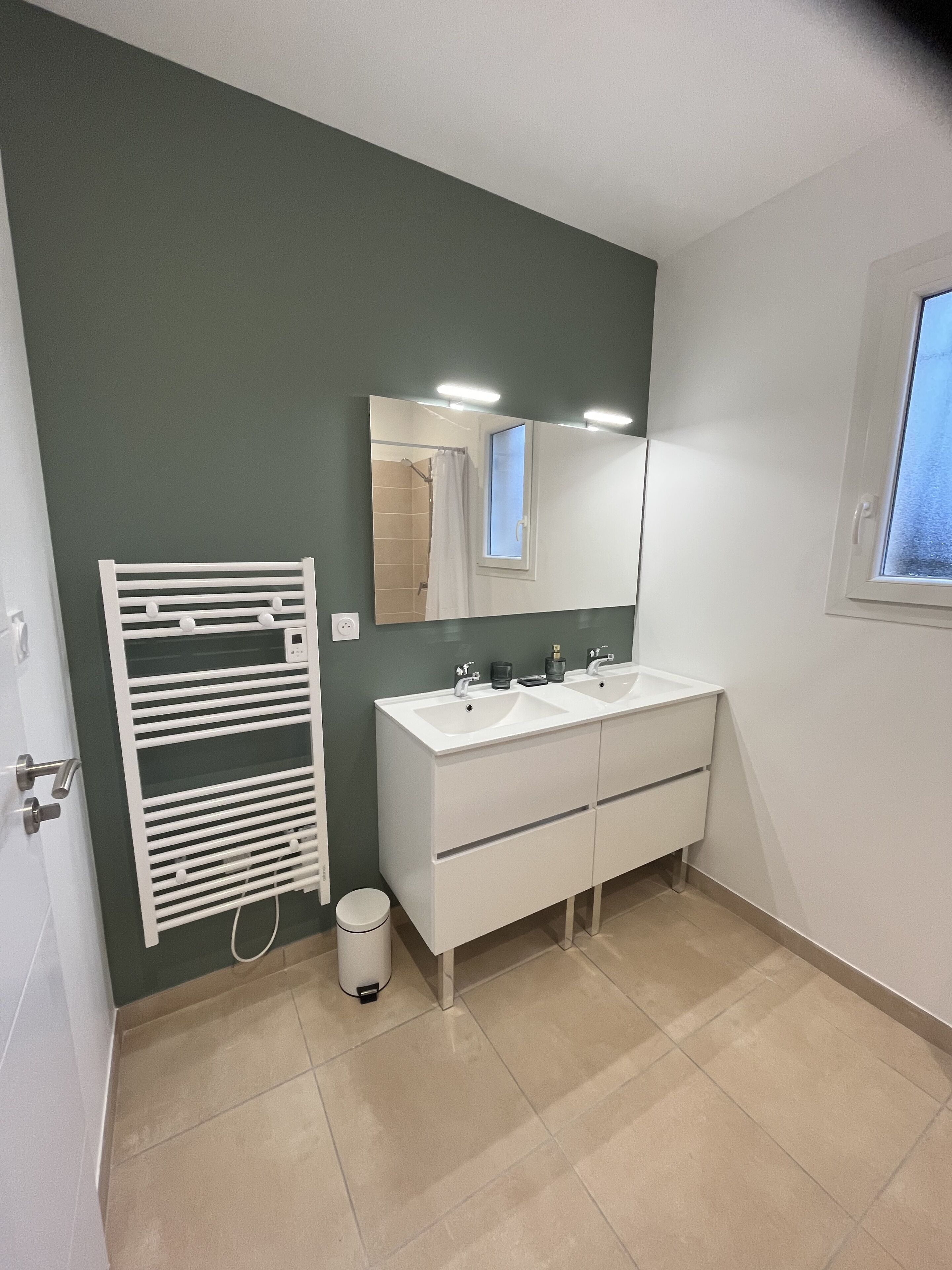 Une salle de bain avec un meuble-lavabo blanc, deux vasques, un miroir et un porte-serviettes.