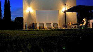 Een gebouw met twee verdiepingen, een garagepoort, twee ramen en een terras met stoelen en een tafel.
