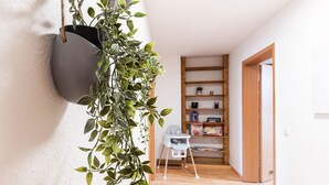 Un pasillo con un colgante gris para plantas con follaje verde, una silla blanca para bebé y una estantería de madera.