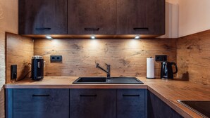 Una cocina moderna con armarios oscuros, encimera de madera, un lavabo y una tetera.