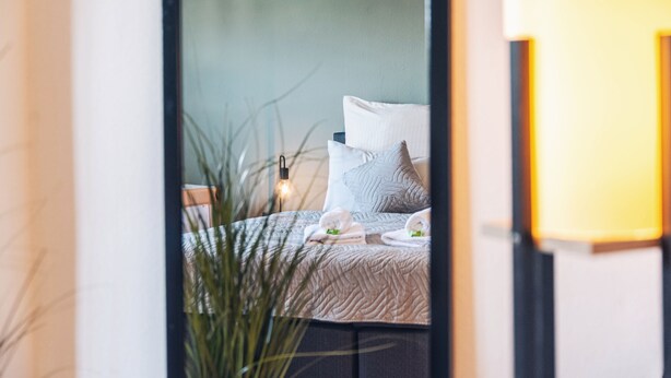 Un dormitorio con cama, almohadas y mesita de noche con lámpara.