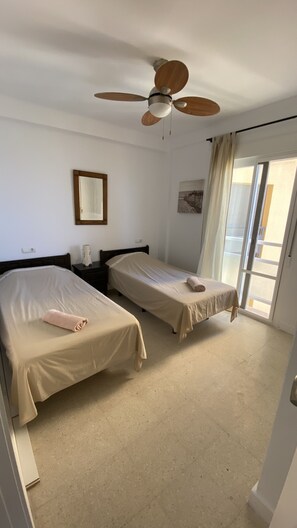 Hotellihuone, jossa on kaksi sänkyä, kattotuuletin, suuri ikkuna verhoilla ja seinälle kiinnitetty peili.