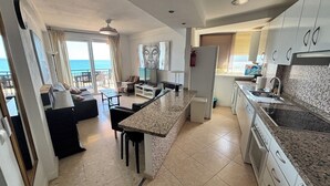 Una cocina moderna con una isla central, un área de comedor con un sofá y sillas, y vistas al mar a través de amplios ventanales.