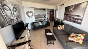 Un soggiorno con TV, divano, tavolino e una cucina sullo sfondo.