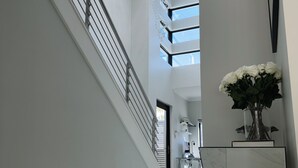 Un passadís ampli i modern amb terra de marbre, una escala amb barana de metall i un llum ornamental.