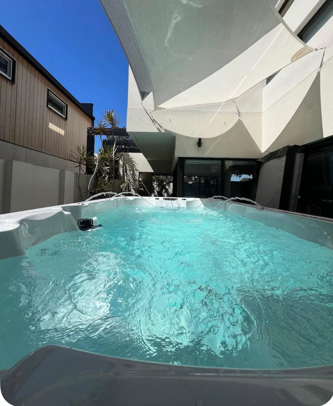 Une piscine recouverte d’une bâche blanche, entourée d’un bâtiment moderne et surplombée par un ciel bleu clair.