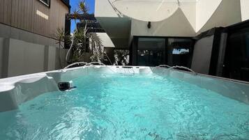 Une piscine recouverte d’une bâche blanche, entourée d’un bâtiment moderne et surplombée par un ciel bleu clair.