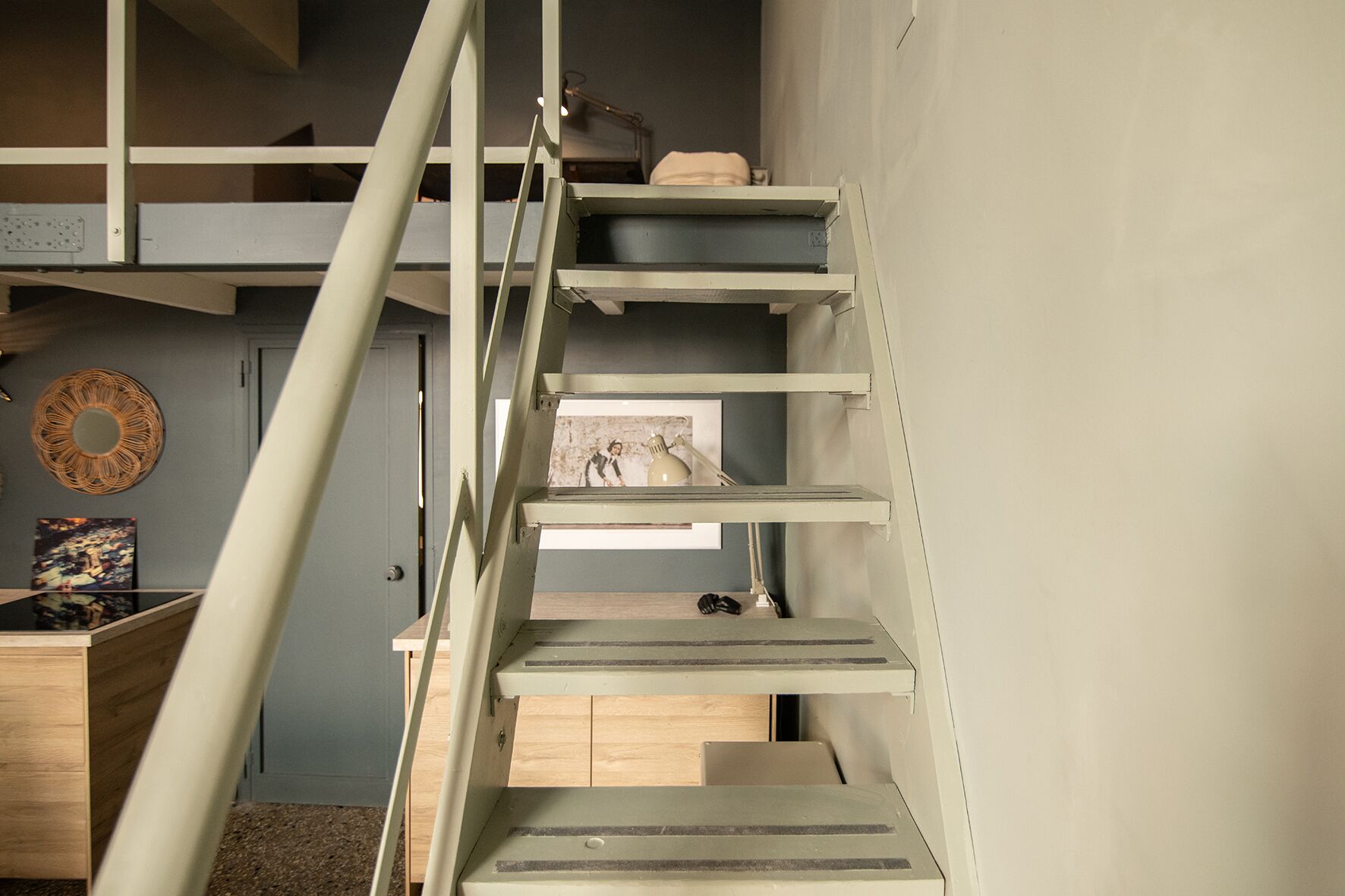 Un intérieur à plusieurs niveaux, avec un escalier, un bureau en bois et une étagère fixée au mur.