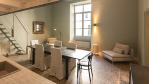 Un comedor con mesa y sillas, una escalera, un sofá y una ventana con luz natural.