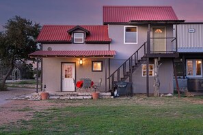 A two-story house with a red roof, a front porch with a table and chairs, and a staircase leading to an upper level.