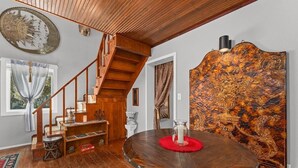 Una escalera de madera, una mesa redonda para comer con un mantelino rojo y un panel decorativo en la pared.