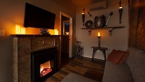 Una sala de estar acogedora con una chimenea de piedra, un televisor de pantalla plana montado encima y un fuste de chimenea con velas.