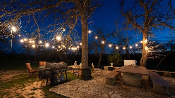 Un patio al aire libre con una parrilla, asientos e iluminación colgante.