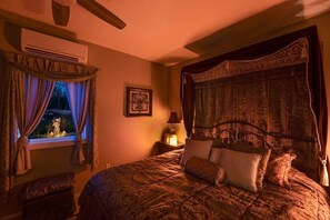Ein Schlafzimmer mit einem großen Bett, einem Nachttisch mit Lampe, einem Fenster mit Vorhängen und einem Wandbild.
