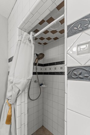 A bathroom with white tiled walls, a shower with a white curtain, and a small shelf with toiletries.