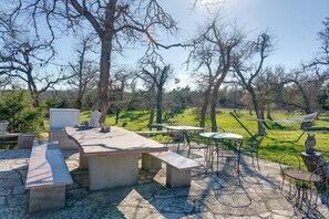 Eine Terrasse im Freien mit Steintischen und -bänken, umgeben von Bäumen und einer grünen Wiese.