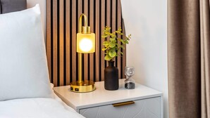 Un lit bien fait, avec du linge de lit blanc, une lampe de chevet, une petite plante en pot et un vase décoratif sur une table de chevet.