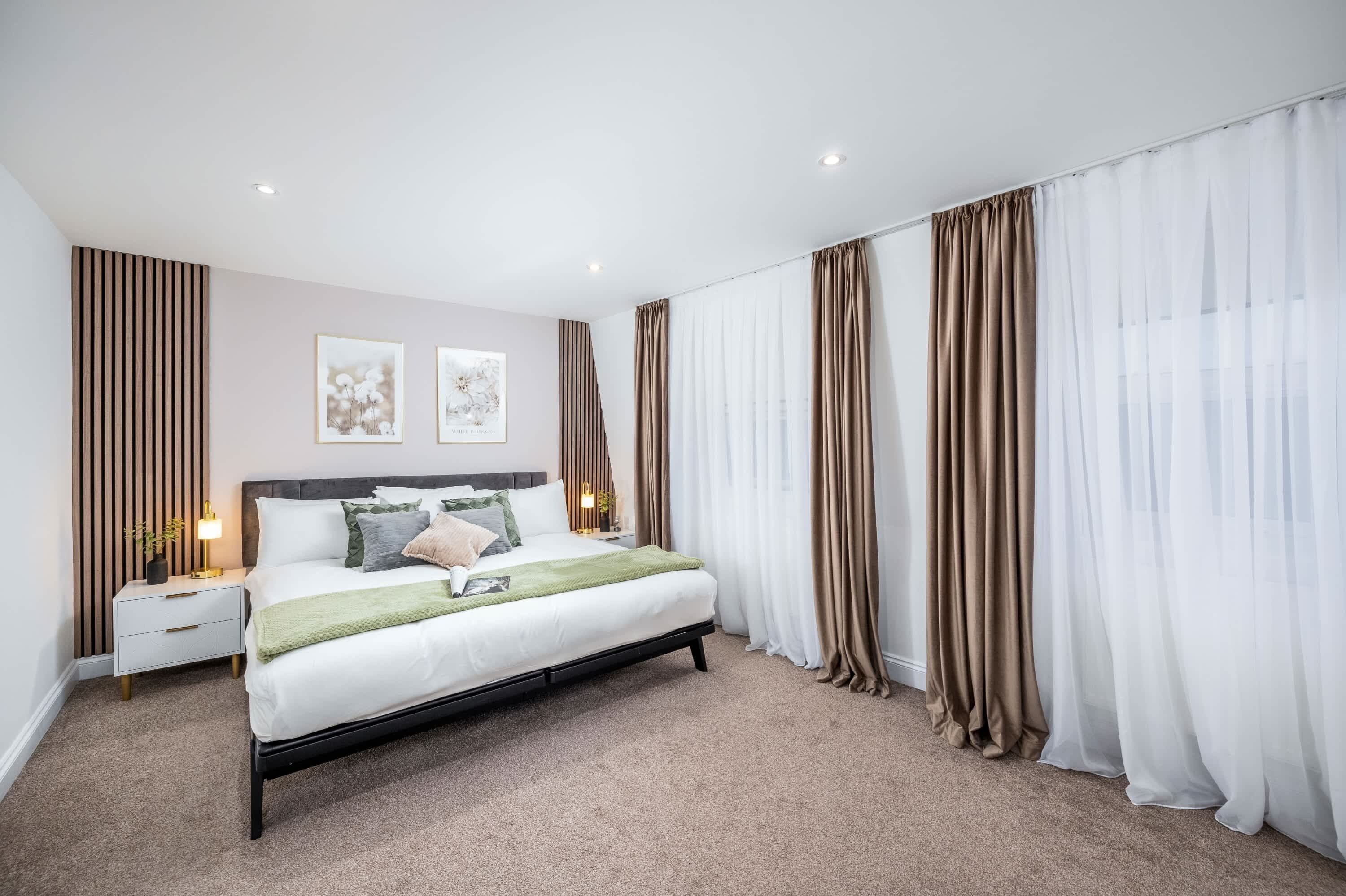 A modern bedroom with a bed, bedside tables, and curtains.