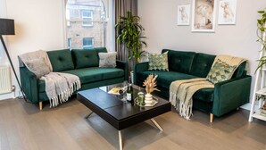 Un salon moderne avec deux canapés verts, une table basse noire et une grande fenêtre avec des rideaux.