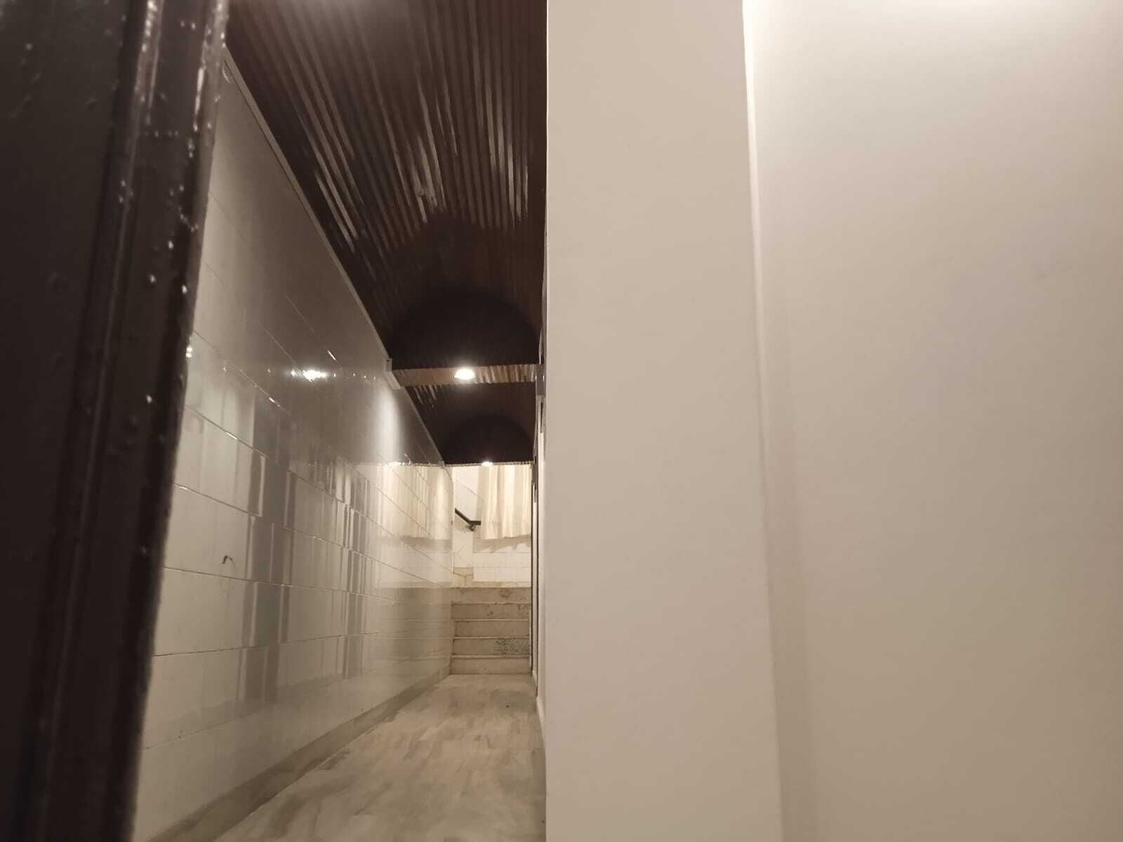 A narrow hallway with tiled walls and a concrete floor, leading to a staircase.