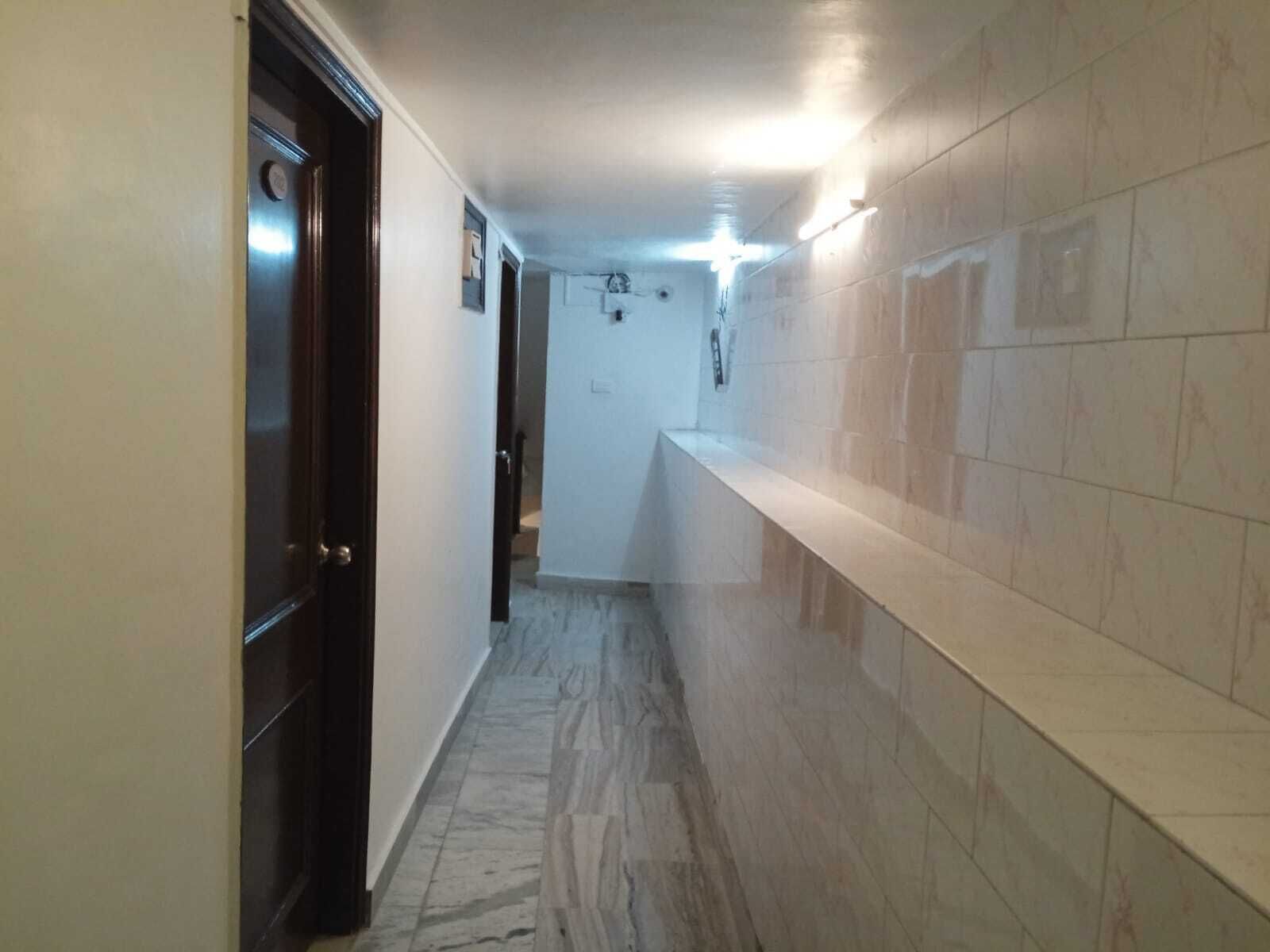 Un pasillo estrecho con suelo de mármol, una puerta oscura a la izquierda y una pared blanca con un accesorio de iluminación a la derecha.