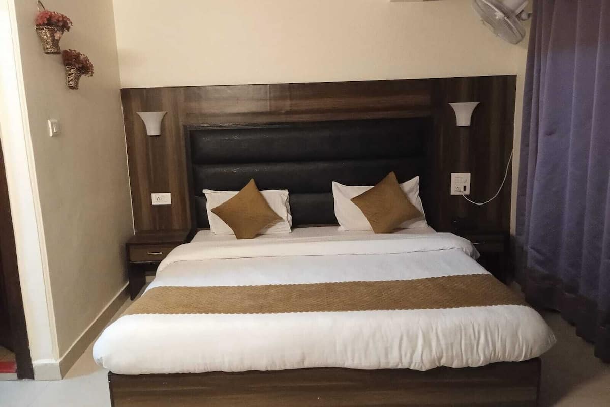 Una cama bien hecha con un cabecero oscuro, dos mesitas de noche y un ventilador de pared.