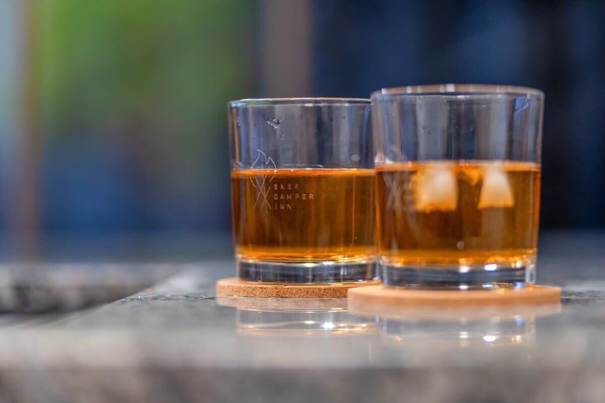 Two glasses of amber liquid on a reflective surface with a blurred background.